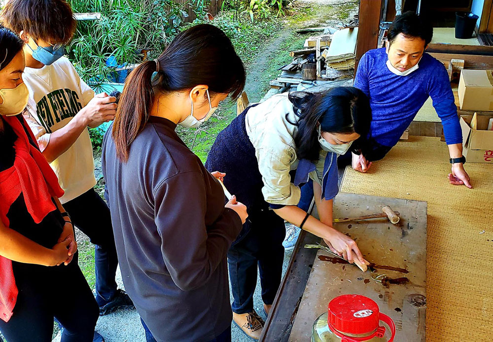 青山さん（右から２人目）からコウゾの木の皮のなめし方を教わる